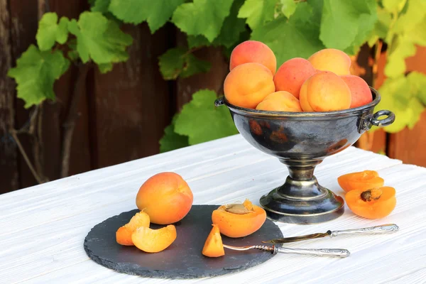 Apricots in a metal vase on a white wooden table — Stock Photo, Image