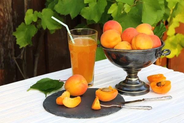 Apricots in a metal vase and a glass of apricot juice — Stock Photo, Image