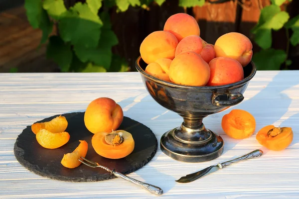 Apricots in a metal vase on a white wooden table — Stock Photo, Image