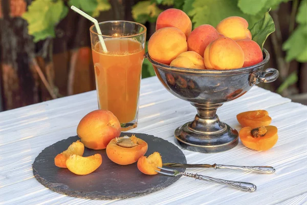 Apricots in a metal vase and a glass of apricot juice — Stock Photo, Image