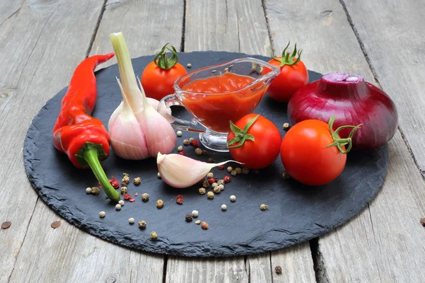 Ketchup chili in a glass gravy boat and its ingredients on a bla — Stock Photo, Image