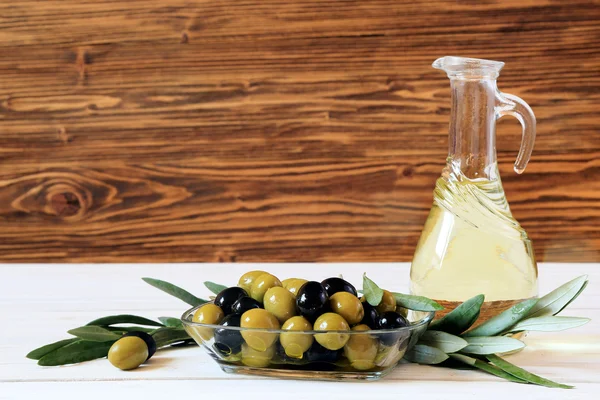 Olives and olive oil on a white table on wooden background — Stock Photo, Image