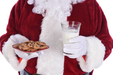 Noel Baba 'nın elinde bir tabak çikolata parçalı kurabiye ve bir bardak süt tutarken ki fotoğrafı..