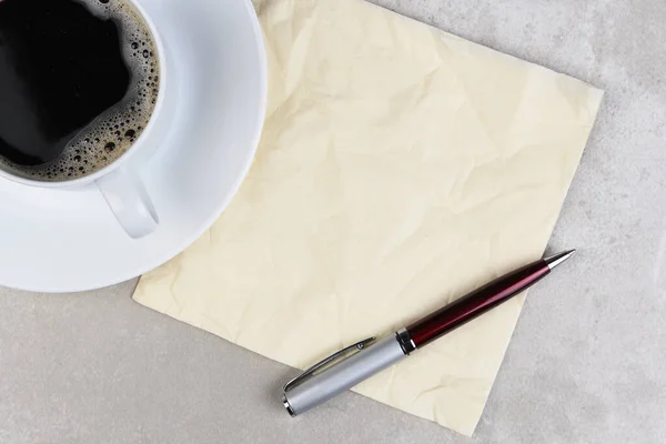一杯咖啡 上面有皱巴巴的餐巾和笔 放在浅灰色的桌子上 — 图库照片