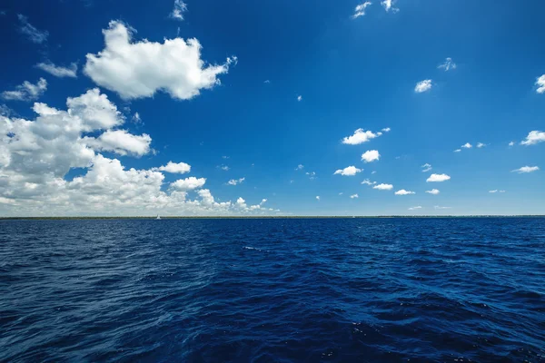 White fluffy clouds blue sky above a surface of the sea — Stock Photo, Image