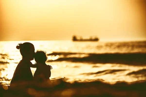 Силуэт маленькой девочки, играющей у моря на закате — стоковое фото