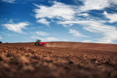 Farmer with tractor seeding crops at field clipart