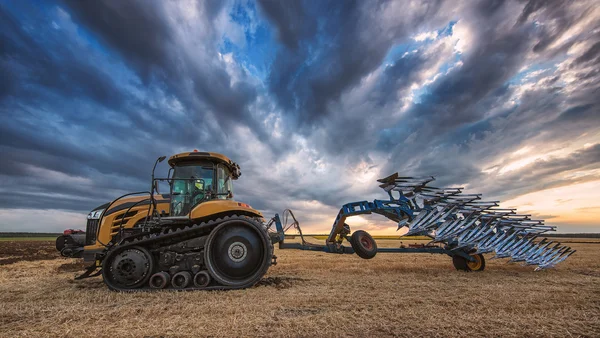 Traktor med plog, plöjning i ett fält — Stockfoto