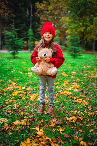 幸せな女の子遊びとともに彼のテディベアおもちゃで秋の公園 — ストック写真