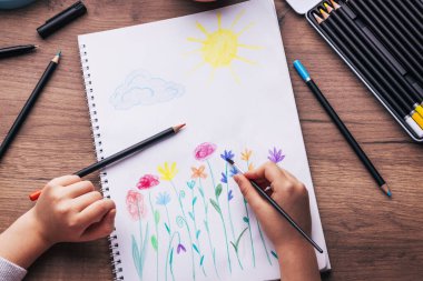 Çocuk üst görünümü çiziyor. Yaratıcı aksesuarları olan bir iş yeri. Masanın üzerinde kızının çizimleri olan çizim tablosu