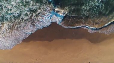Sahile vuran deniz dalgalarının havadan görünüşü. 4k videosunda mavi su arkaplanı