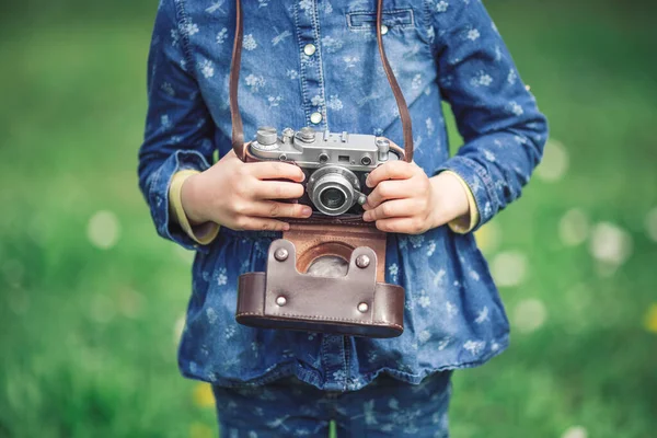 Eski model fotoğraf makinesi olan küçük bir kız parkta doğanın fotoğraflarını çekiyor.