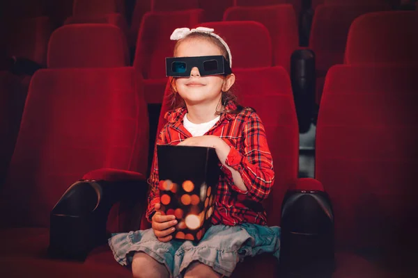 Little girl watching cartoon 3D movie in cinema and eating popcorn