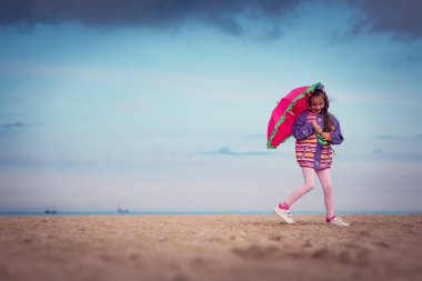 Sahilde duran şemsiyeli kız.