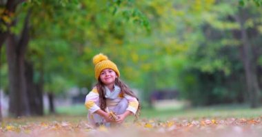Küçük çocuk sonbahar ağaçlarında ve sonbahar mevsiminde eğleniyor. Kız düşen yapraklarla oynuyor..