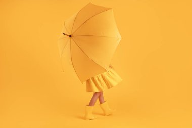 Sarı arka planda yağmur ve şemsiye için lastik çizmeli kız