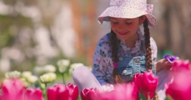 Bahar lalelerinden ve renkli çiçeklerden oluşan renkli bahçeye gülümseyen güzel küçük kız.