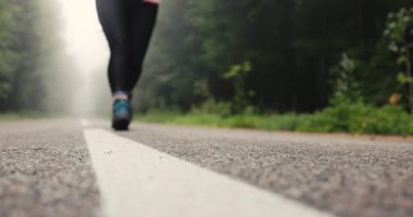 Ormanın yanındaki sisli dağ yolunda yürüyüş botları ve spor malzemeleriyle koşan genç bir turist kadın.