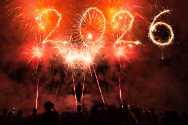 Yeni yıl 2026 Bengal ışıkları ve gece gökyüzünde parlayan havai fişekler ve insanların siluetlerini kutlayan kalabalık.