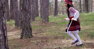 Etnik folklor kostümlü Bulgar kız ormanda ağaçların arkasında koşuyor, Bulgar güzel doğası ve Bulgar ruhunun özgürlüğü