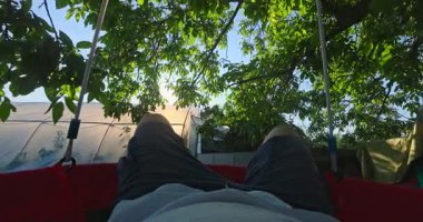 Adam ağaçta sallanıyor, dışarıda sallanıyor, rahatlıyor ve kırsalda güzel bir günün ve doğanın tadını çıkarıyor.