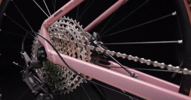 Arka dişli kaset ve lastik dönüşünü gösteren bisiklet mekanizması yakın plan. Siyah arka planda izole edilmiş bisiklet stüdyosu için pembe çerçevede zincir ve raydan çıkarıcı.