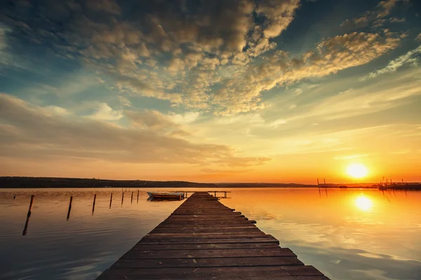 Barco e molhe no lago com um reflexo na água ao pôr do sol — Fotografia de Stock