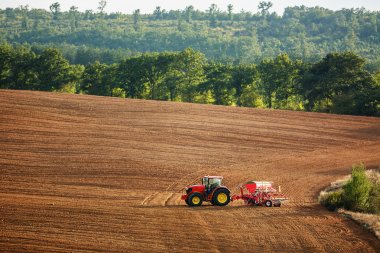 Farmer with tractor seeding crops at field