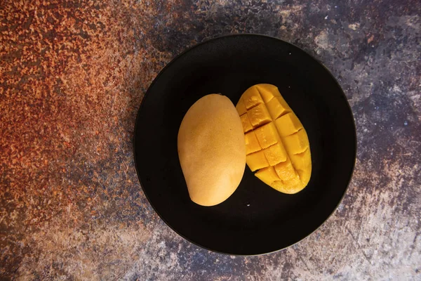 Fruta de manga amarela fresca em um prato preto — Fotografia de Stock