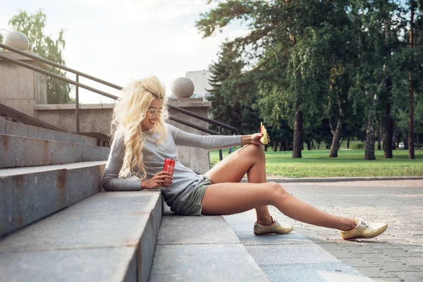 Belleza rubia joven mujer sentado en al aire libre y comer — Foto de Stock