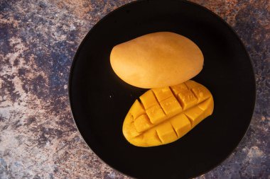 Siyah tabakta taze sarı mango meyvesi.