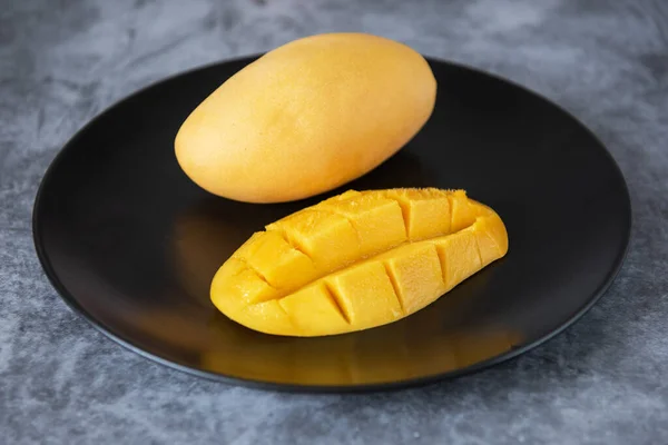 Fruta de manga amarela fresca em um prato preto — Fotografia de Stock
