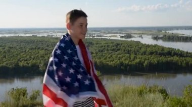 Sarışın çocuk nehir kıyısında mavi gökyüzünde ulusal Amerikan bayrağı sallıyor.