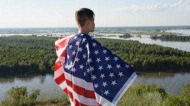 Sarışın çocuk nehir kıyısında mavi gökyüzünde ulusal Amerikan bayrağı sallıyor.