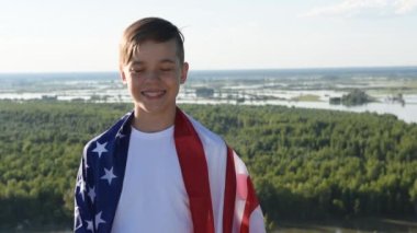 Sarışın çocuk nehir kıyısında mavi gökyüzünde ulusal Amerikan bayrağı sallıyor.
