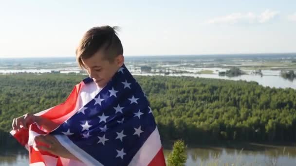 Ragazzo biondo sventola bandiera nazionale USA all'aperto sopra il cielo blu sulla riva del fiume — Video Stock