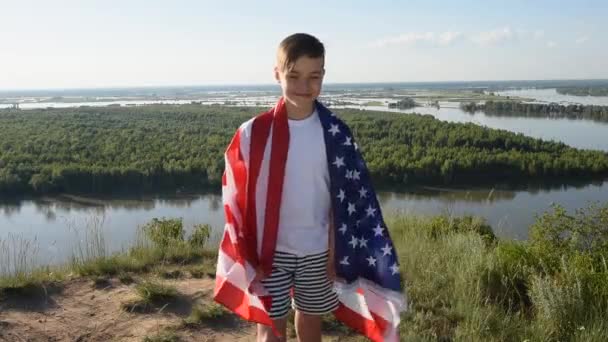 Ragazzo biondo sventola bandiera nazionale USA all'aperto sopra il cielo blu sulla riva del fiume — Video Stock