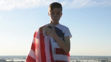 Sarışın çocuk nehir kıyısında mavi gökyüzünde ulusal Amerikan bayrağı sallıyor.