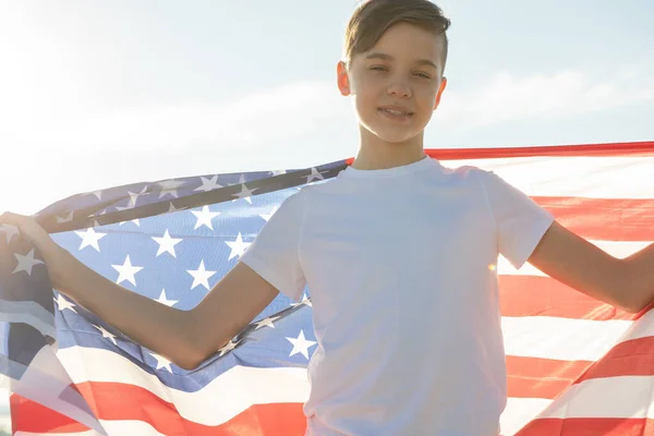 Blonďatý chlapec mává národní vlajkou USA venku nad modrou oblohou na břehu řeky — Stock fotografie