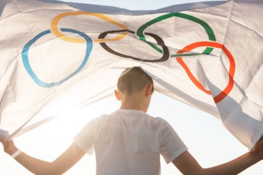 Sarışın çocuk nehir kıyısında açık havada Olimpiyat Oyunları bayrağını sallıyor.
