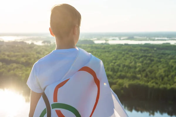 Blonde boy waving waving flag the Olympic Games outdoors over blue sky at the river bank — Stock Photo, Image