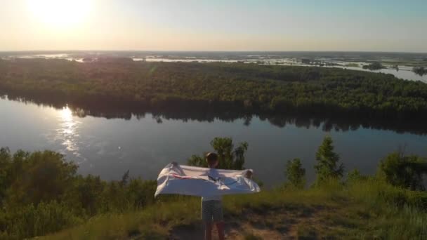 Повітряний дрон 4k відео хлопчика розмахуючи прапором Олімпійські ігри над блакитним небом на березі річки — стокове відео