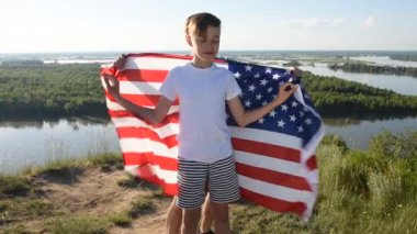 Sarışın çocuk nehir kıyısında mavi gökyüzünde ulusal Amerikan bayrağı sallıyor.