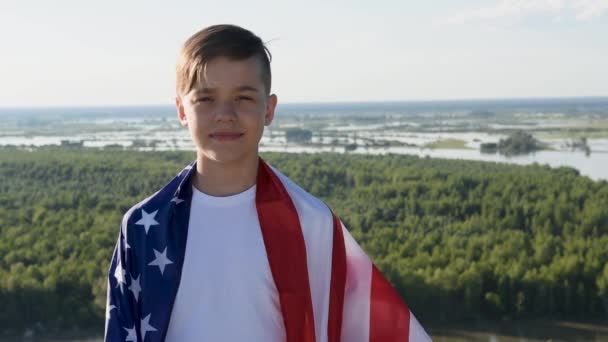 Sarışın çocuk nehir kıyısında mavi gökyüzünde ulusal Amerikan bayrağı sallıyor. — Stok video