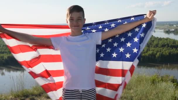 Blonde boy waving national USA flag outdoors over blue sky at the river bank — ストック動画
