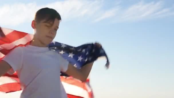 Ξανθό αγόρι κυματίζει εθνική σημαία των ΗΠΑ σε εξωτερικούς χώρους πάνω από τον γαλάζιο ουρανό στην όχθη του ποταμού — Αρχείο Βίντεο