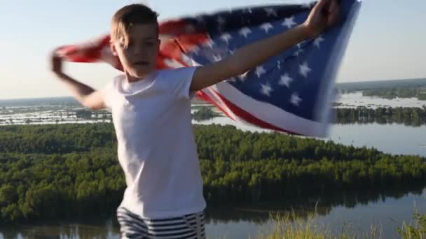 Ragazzo biondo sventola bandiera nazionale USA all'aperto sopra il cielo blu sulla riva del fiume — Video Stock