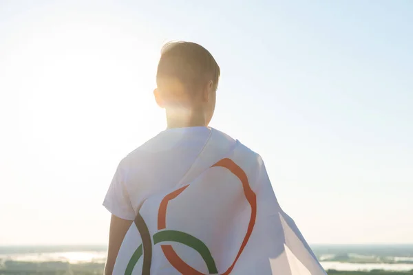 Blonde boy waving waving flag the Olympic Games outdoors over blue sky at the river bank — Stock Photo, Image