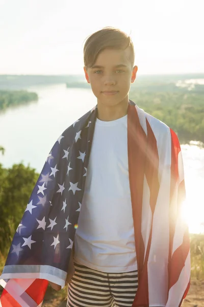 Blondine jongen zwaaien nationale VS vlag buiten boven de blauwe hemel aan de oever van de rivier — Stockfoto