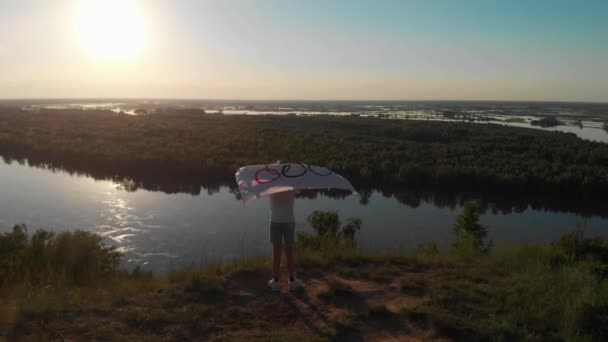 Aerial drone 4k video of boy waving flag the Olympic Games over blue sky at the river bank — Stock Video